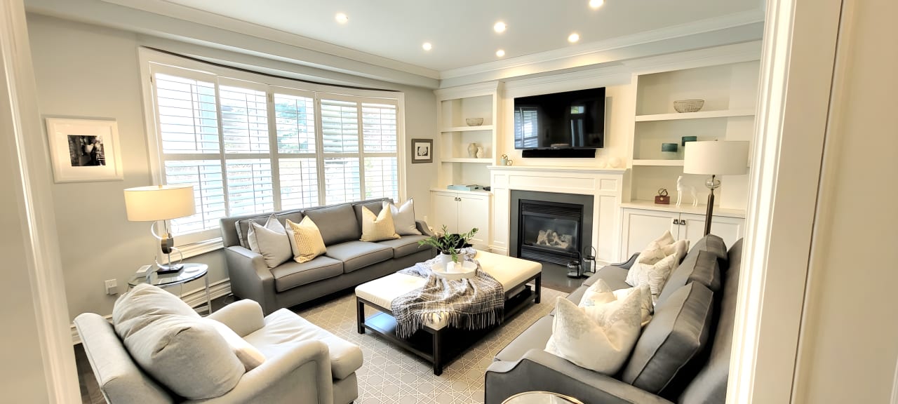 A living room with two gray couches, a chair, a white coffee table, a fireplace, and a flat-screen TV mounted on the wall.