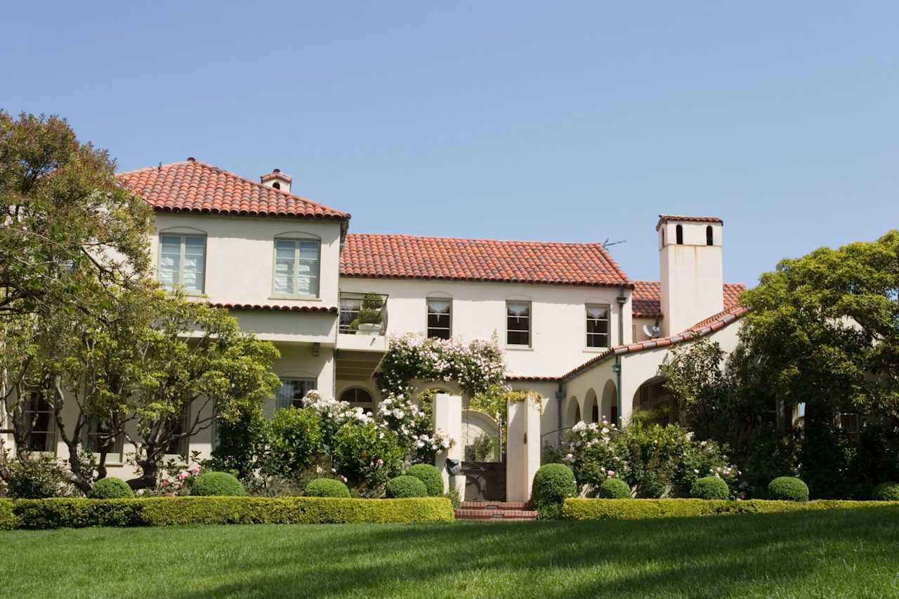 A large white house with a red tile roof. The house has two stories and a black front gate.