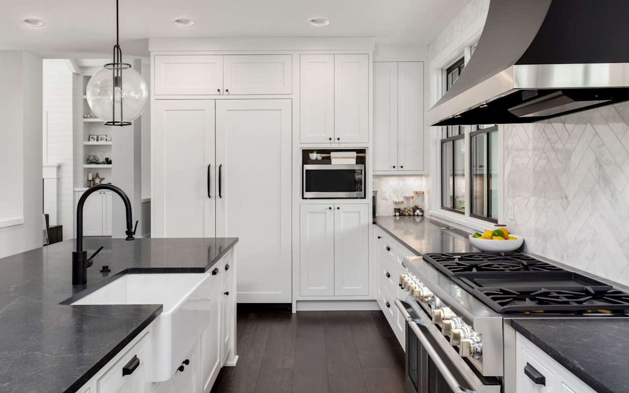 Modern white kitchen with dark stone island, black faucet, and stainless steel range.
