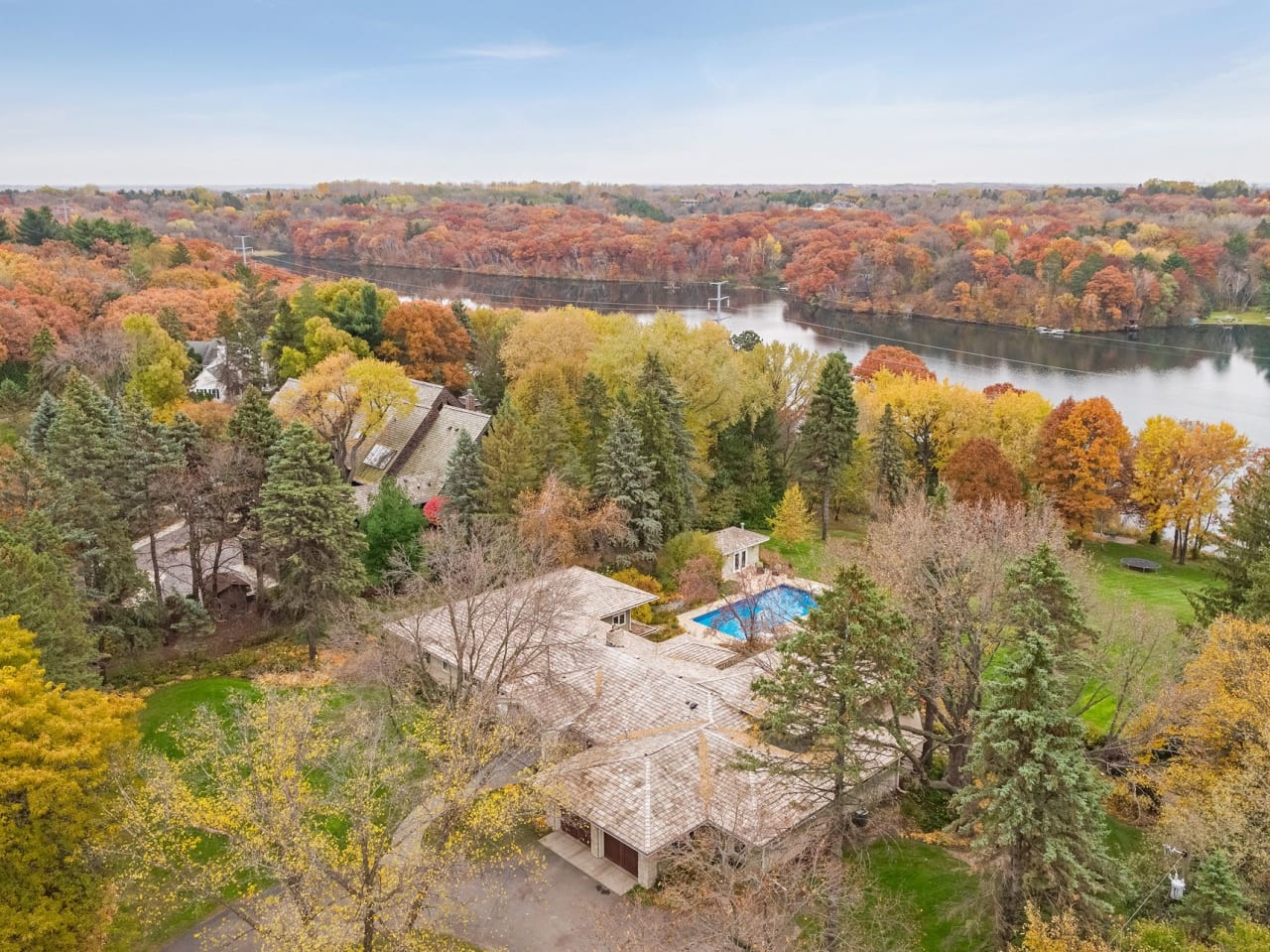 An aerial view of a house with a swimming pool surrounded by trees near the lake.