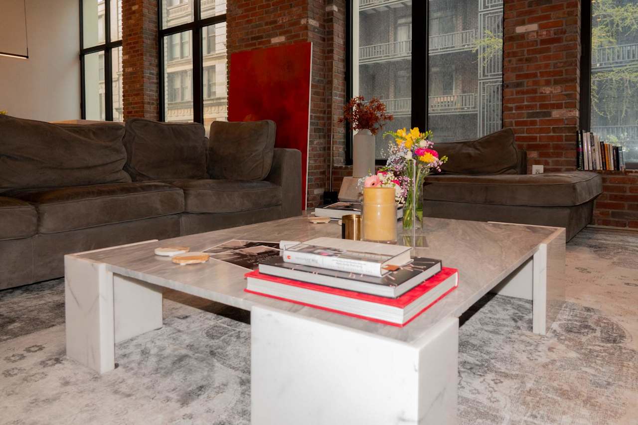 Living room with dark sofas, a marble coffee table, exposed brick, and tall windows.