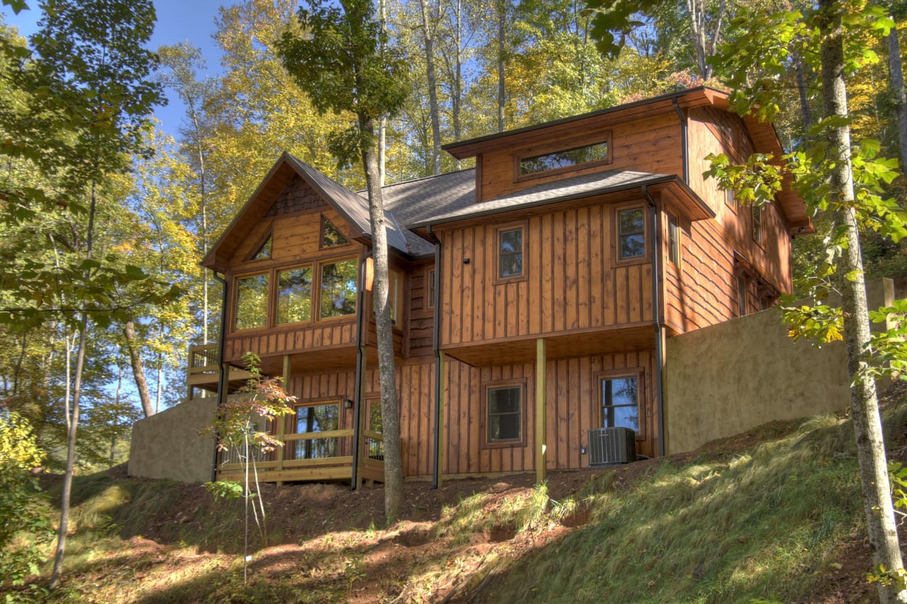 A large log cabin with a  brown roof sits on a hill surrounded by trees.