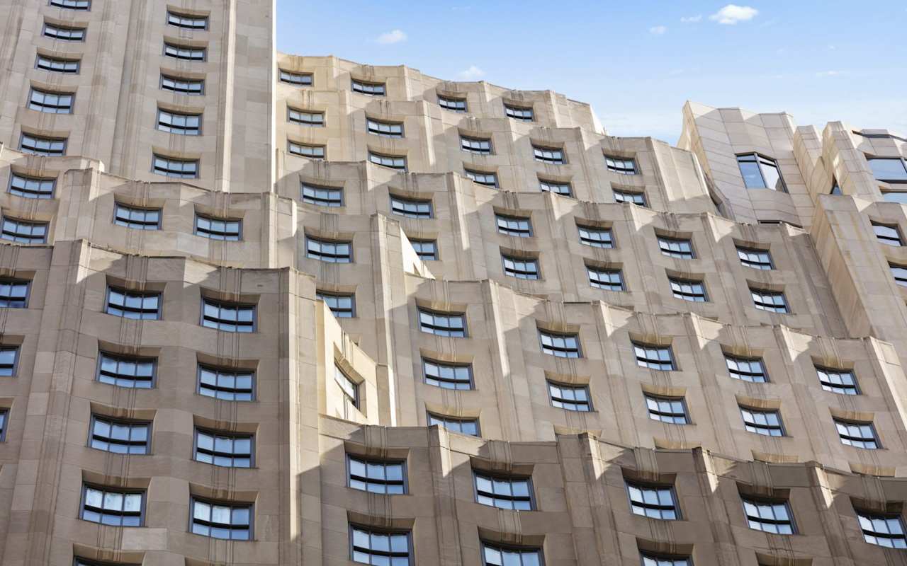 A close-up view of a modern building facade featuring a wavy design and numerous windows against a blue sky.