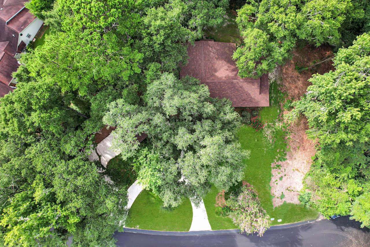 Drone or aerial photo of home featuring a lightly colored roof, circular driveway, and large trees