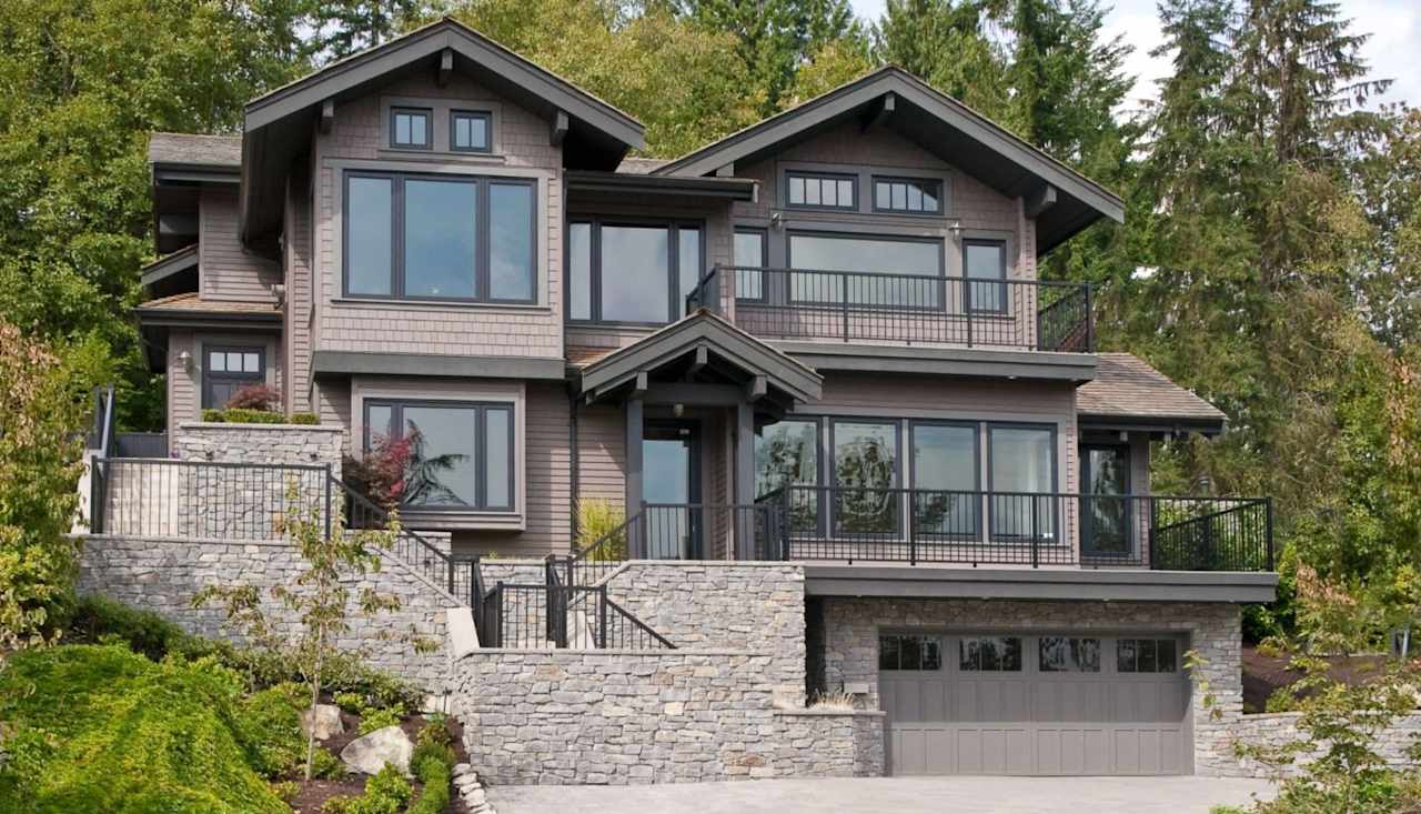 A large gray house with a lot of windows and a garage in the middle of a forest.