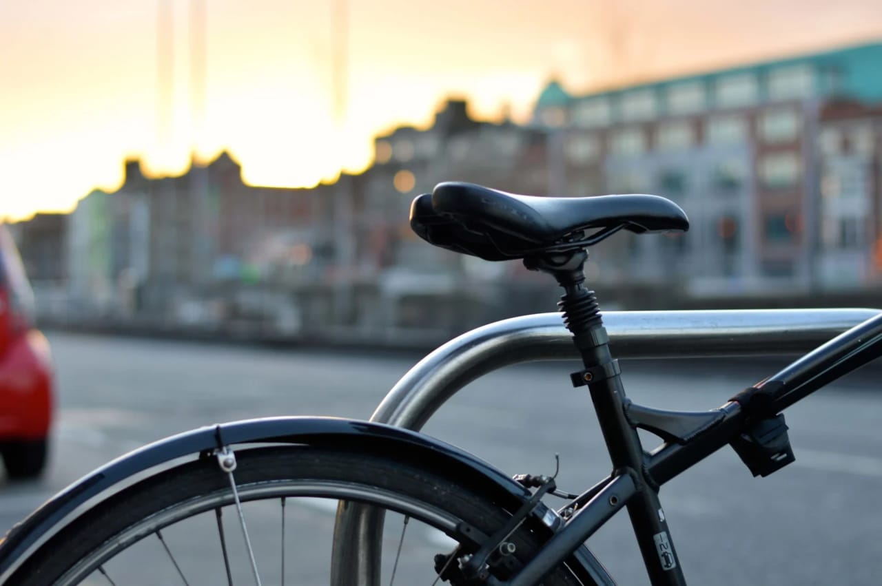 A black bicycle parked in a silver bike rack on a city street at sunset.