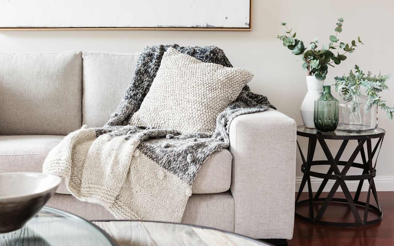Living room with a beige sofa, layered knit throws, and plants on a round side table.