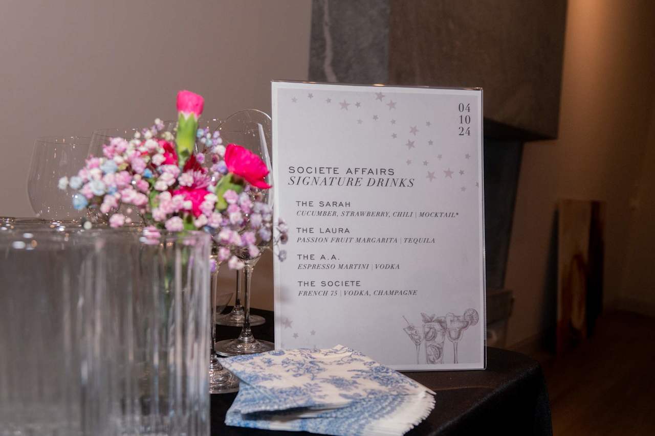 Signature-drinks menu beside pink flowers, glassware, and patterned napkins.