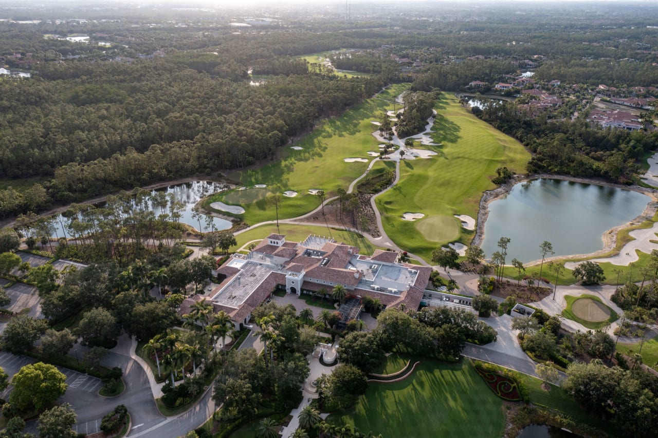 An aerial view of a golf course with a clubhouse in the center and a lake in the background