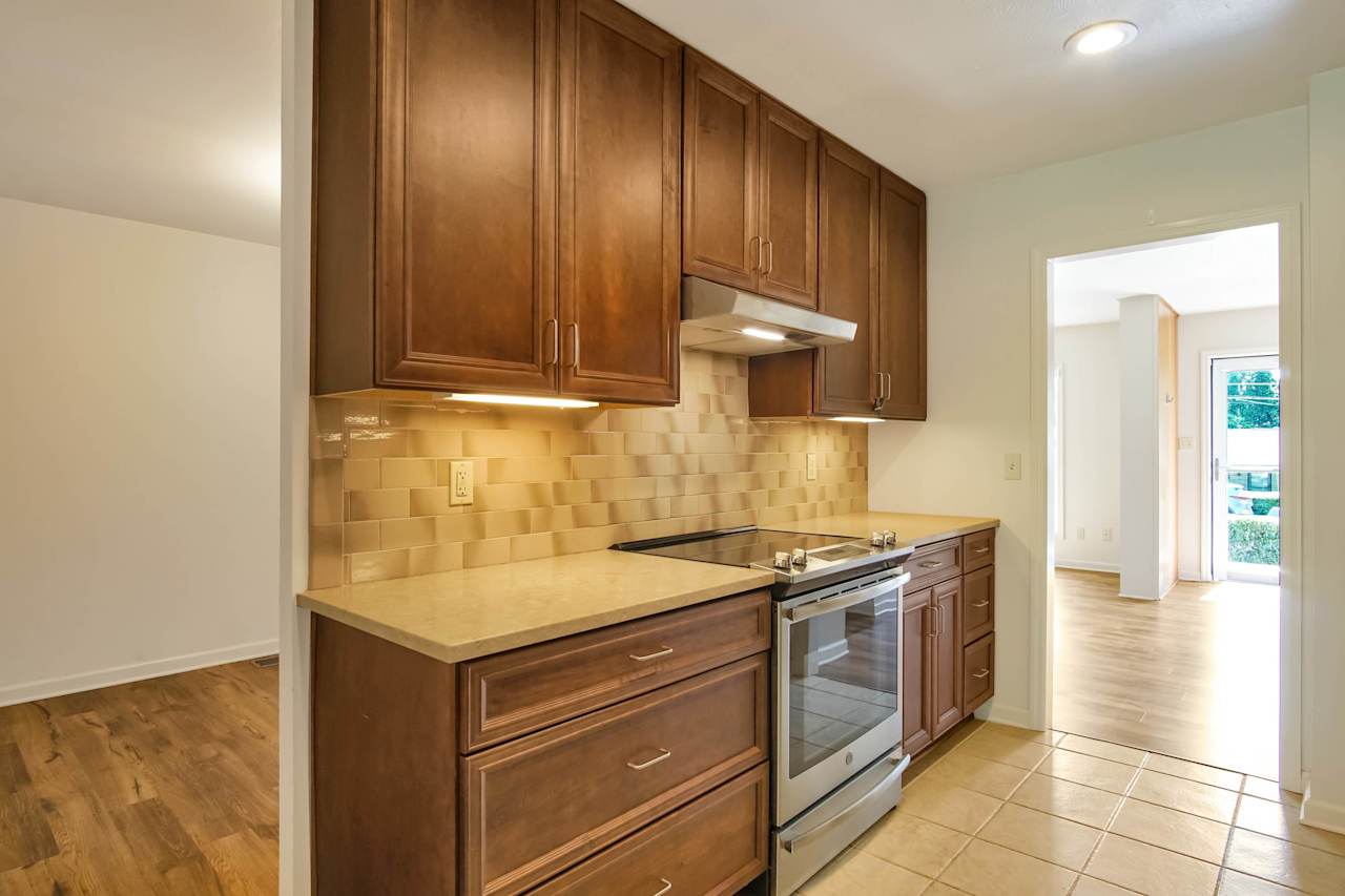 Photo of the kitchen featuring tiled black splash, richwood Cabinets, stainless steel hood, and a stainless steel flat top oven and stove at 1228 Winifred Drive, Tallahassee, Florida 32308