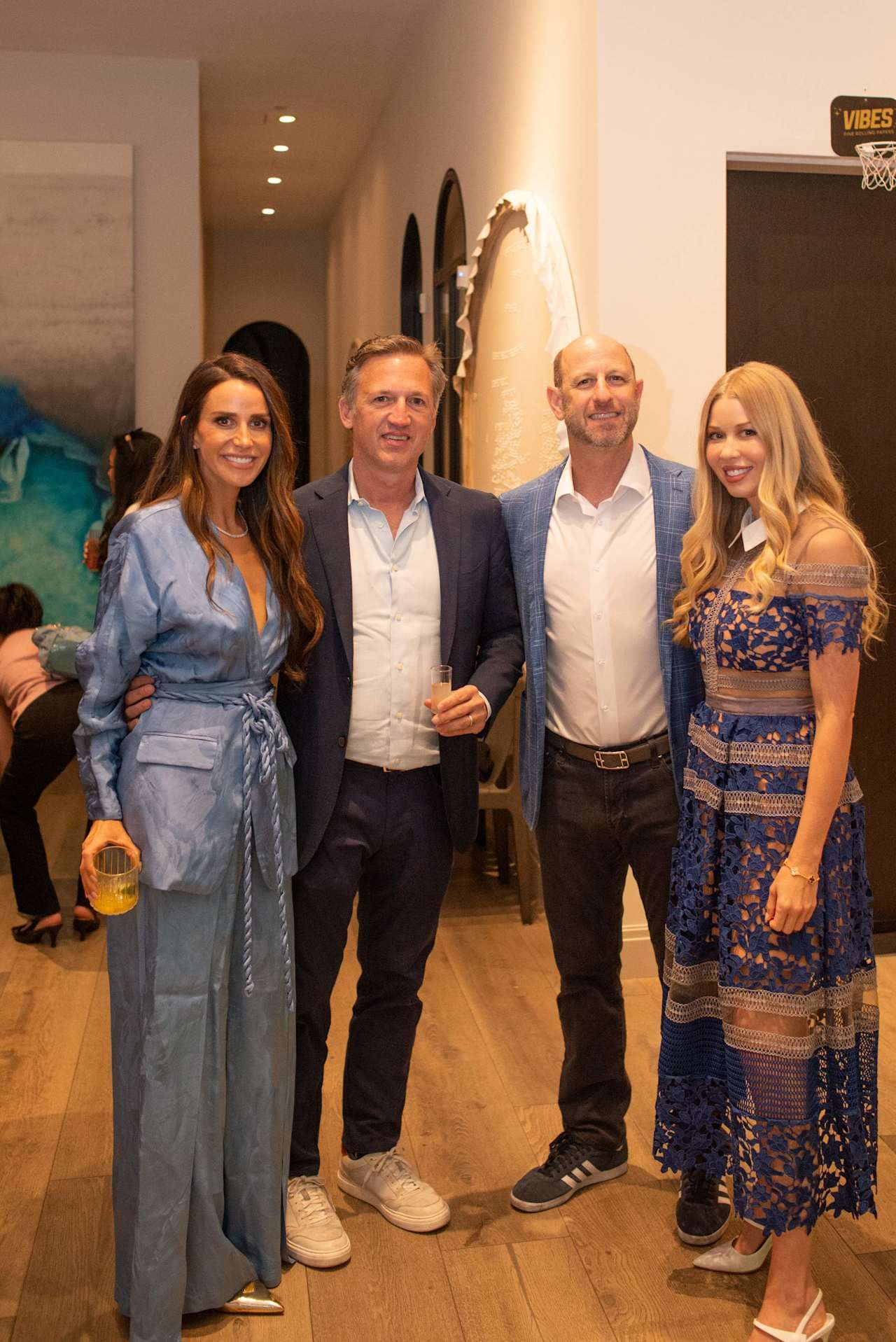 Four adults pose together at an indoor event, with a basketball hoop behind them.