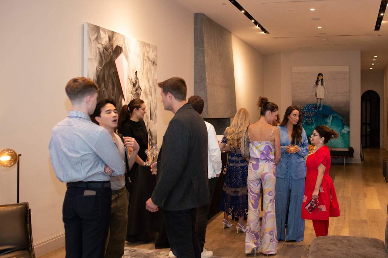Guests mingle at a social gathering among contemporary artwork in a modern interior.