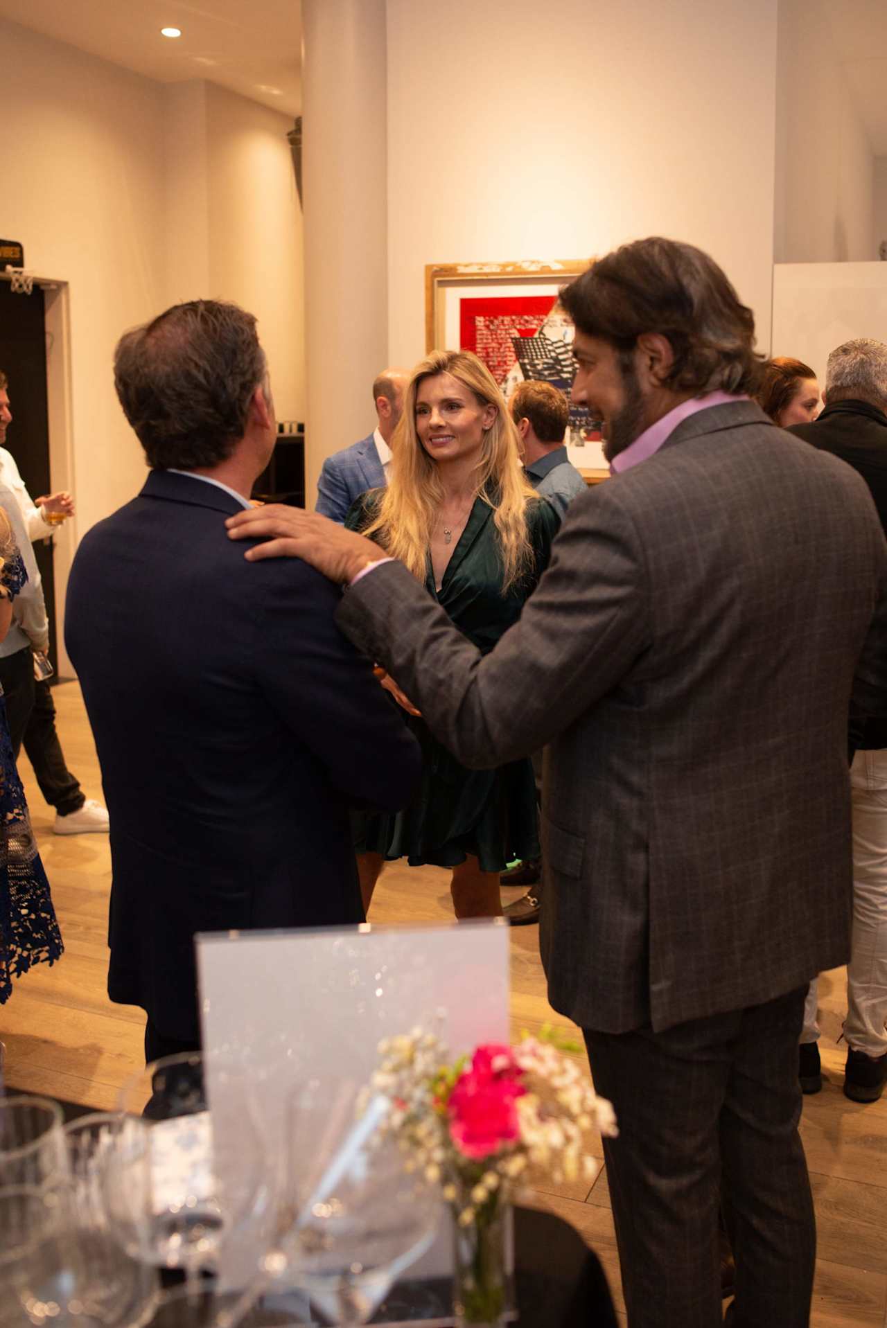 Adults mingle at a reception as a man in a gray suit talks with a blonde woman.
