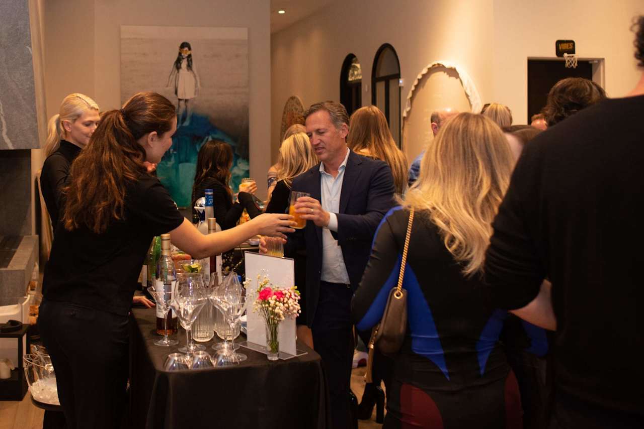 Guests mingle at a reception around a table of drinks and flowers.