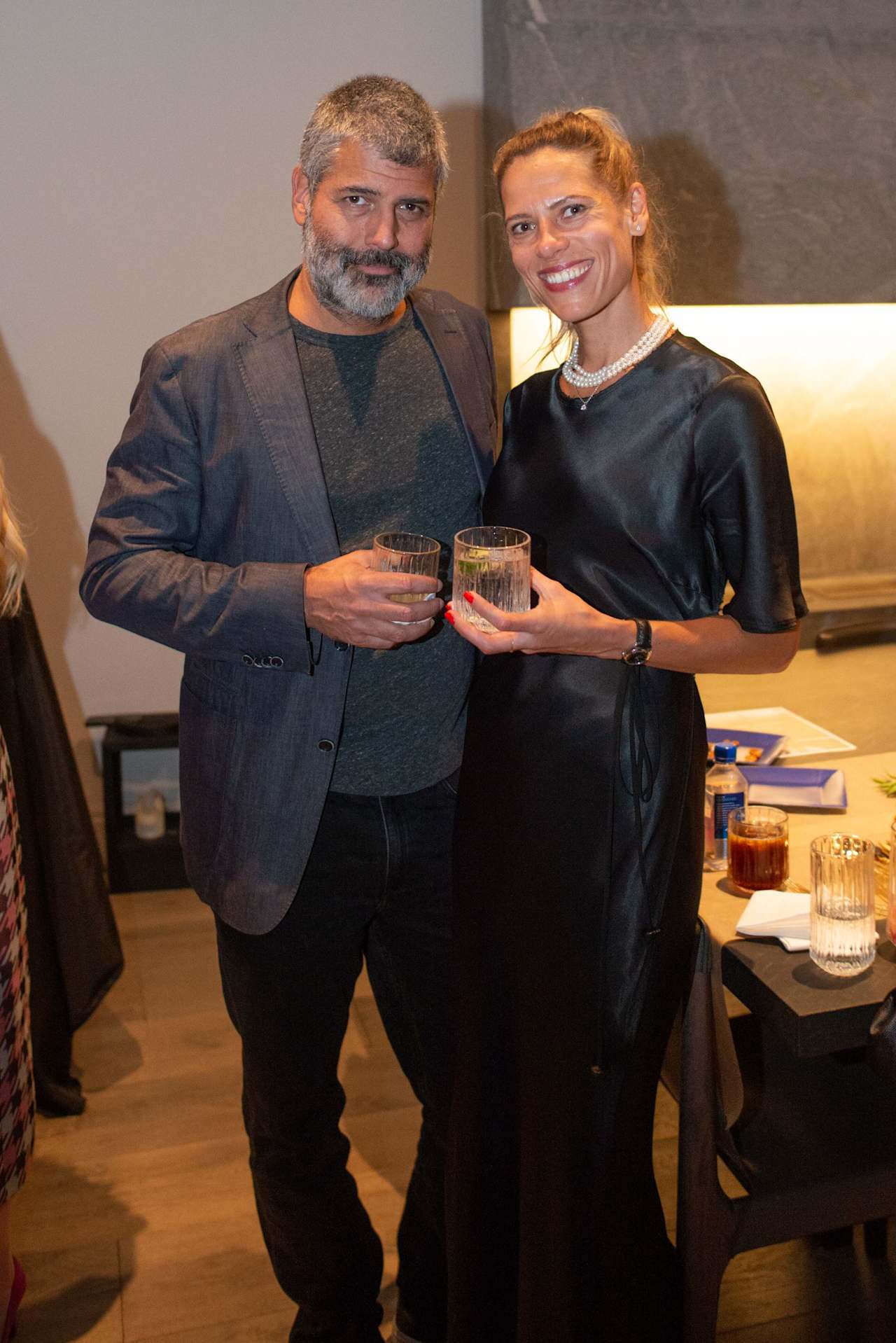 Two adults pose with drinks at an indoor gathering.