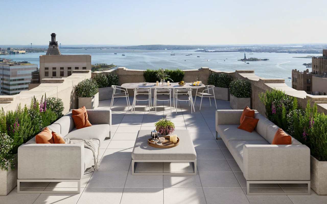 A stylish rooftop terrace with modern furniture, potted plants, and a scenic view of water and distant landmarks.