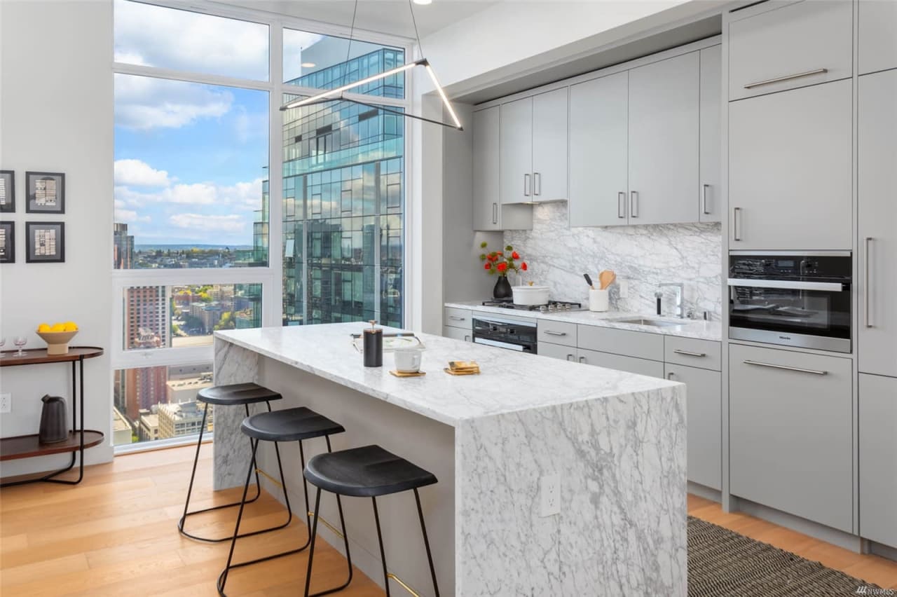 Modern kitchen in a condo with marble countertops and stools.