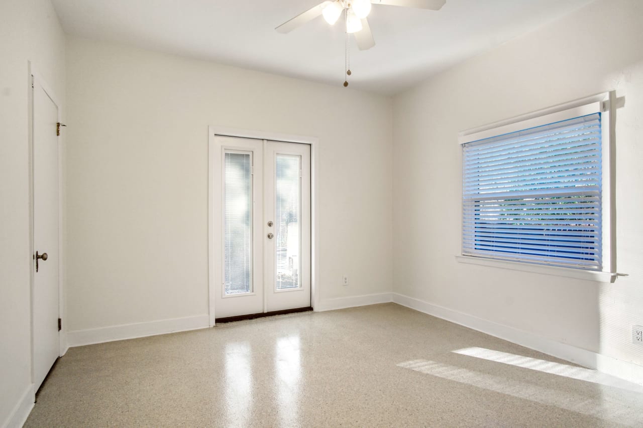 A bedroom with a neutral color palette and large windows. The room appears bright and airy.