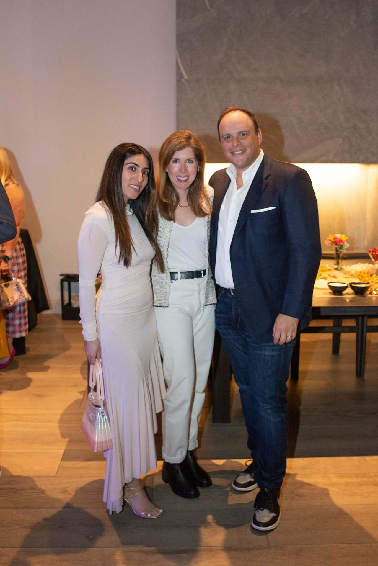 Three people pose together at an indoor event beside a buffet table.