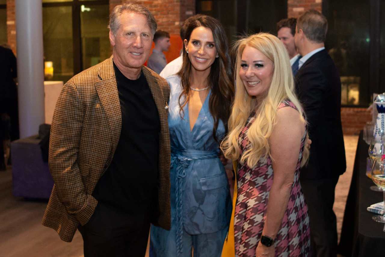 Three guests pose together at an indoor event, with other attendees in the background.