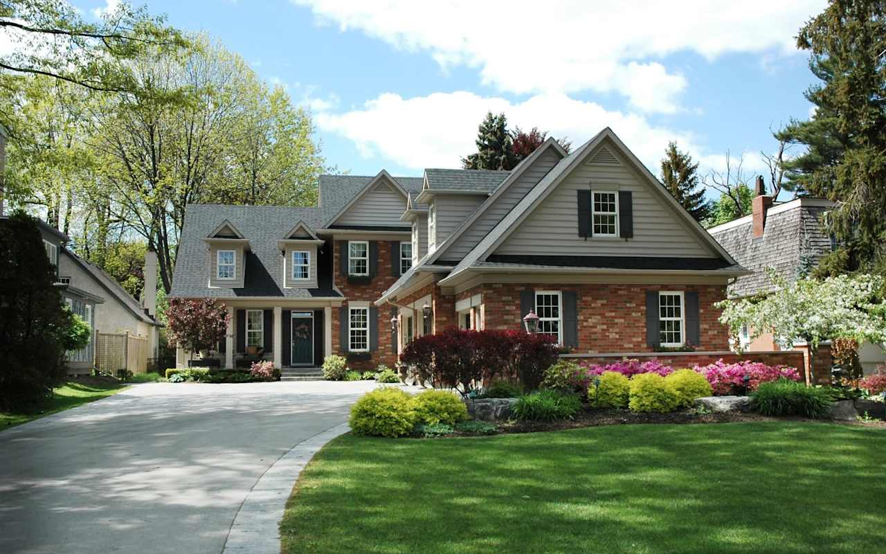 Two-story brick home with gray gables, curved driveway, and flowering front gardens.
