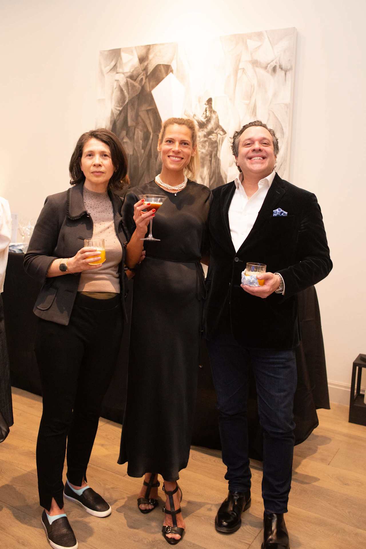 Three adults pose with drinks in front of an abstract painting.