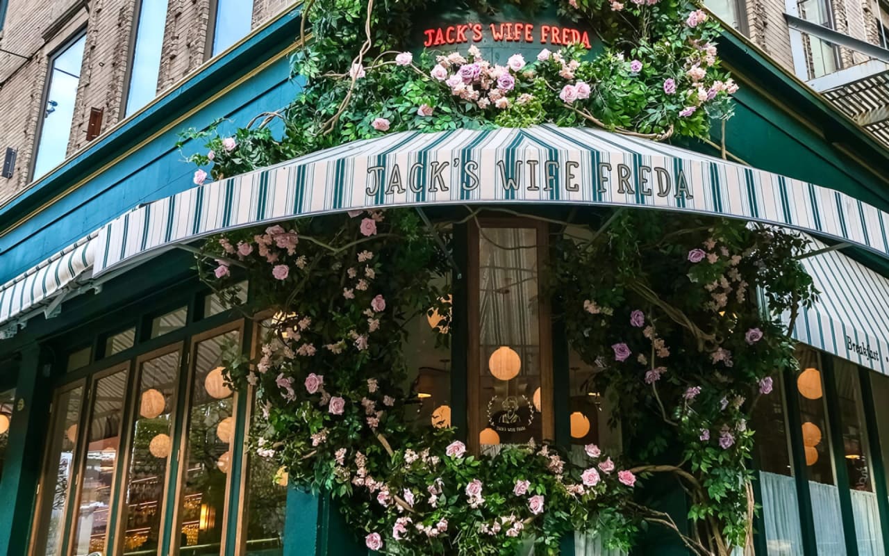 The exterior of Jack's Wife Freda restaurant with a striped awning and a wreath of flowers above the entrance.