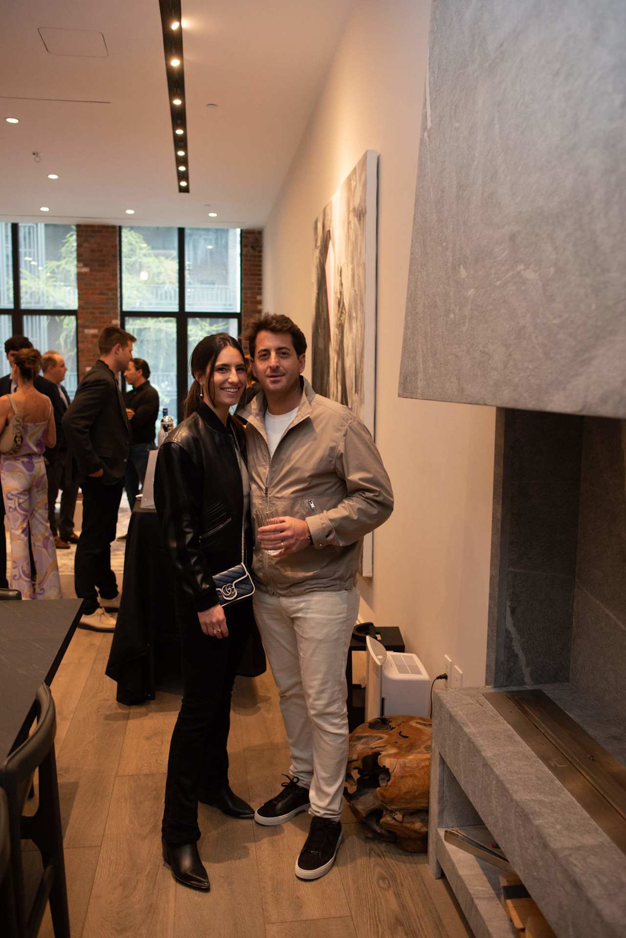 A smiling couple poses together at an art gallery reception as other guests mingle.