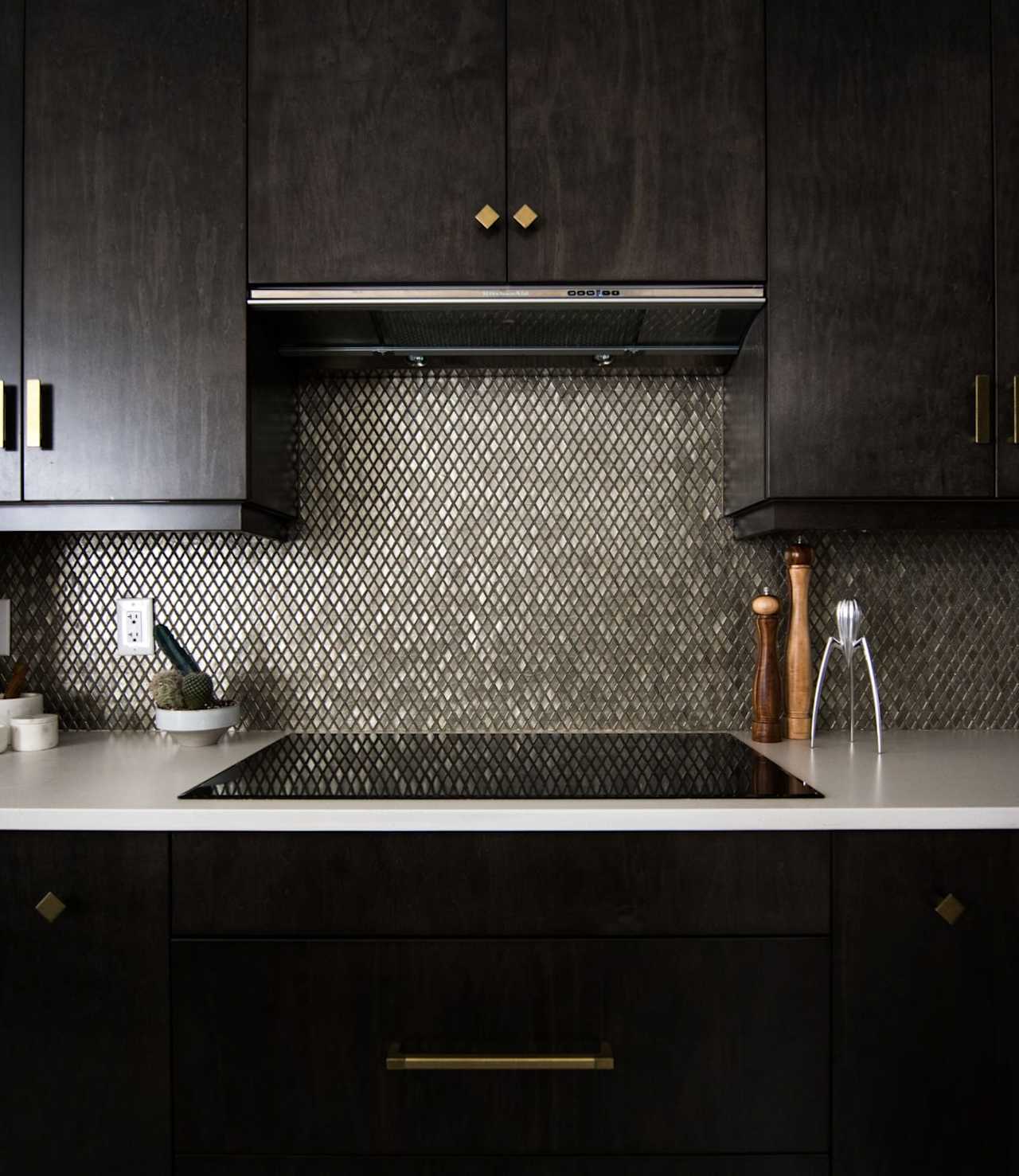 Modern kitchen with dark cabinets, brass hardware, diamond-pattern backsplash, and induction cooktop.