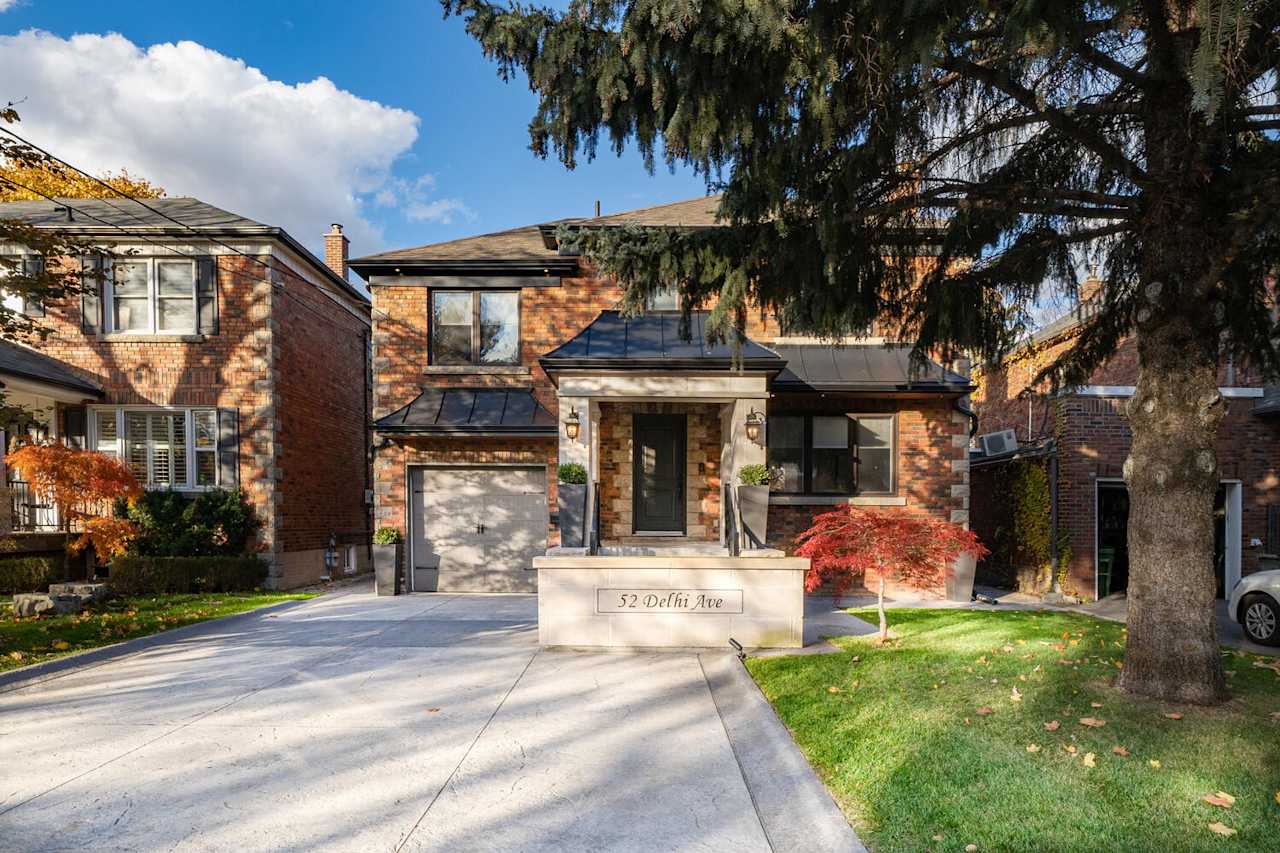 A two-story house with brick exterior and a driveway with a tree in the front yard