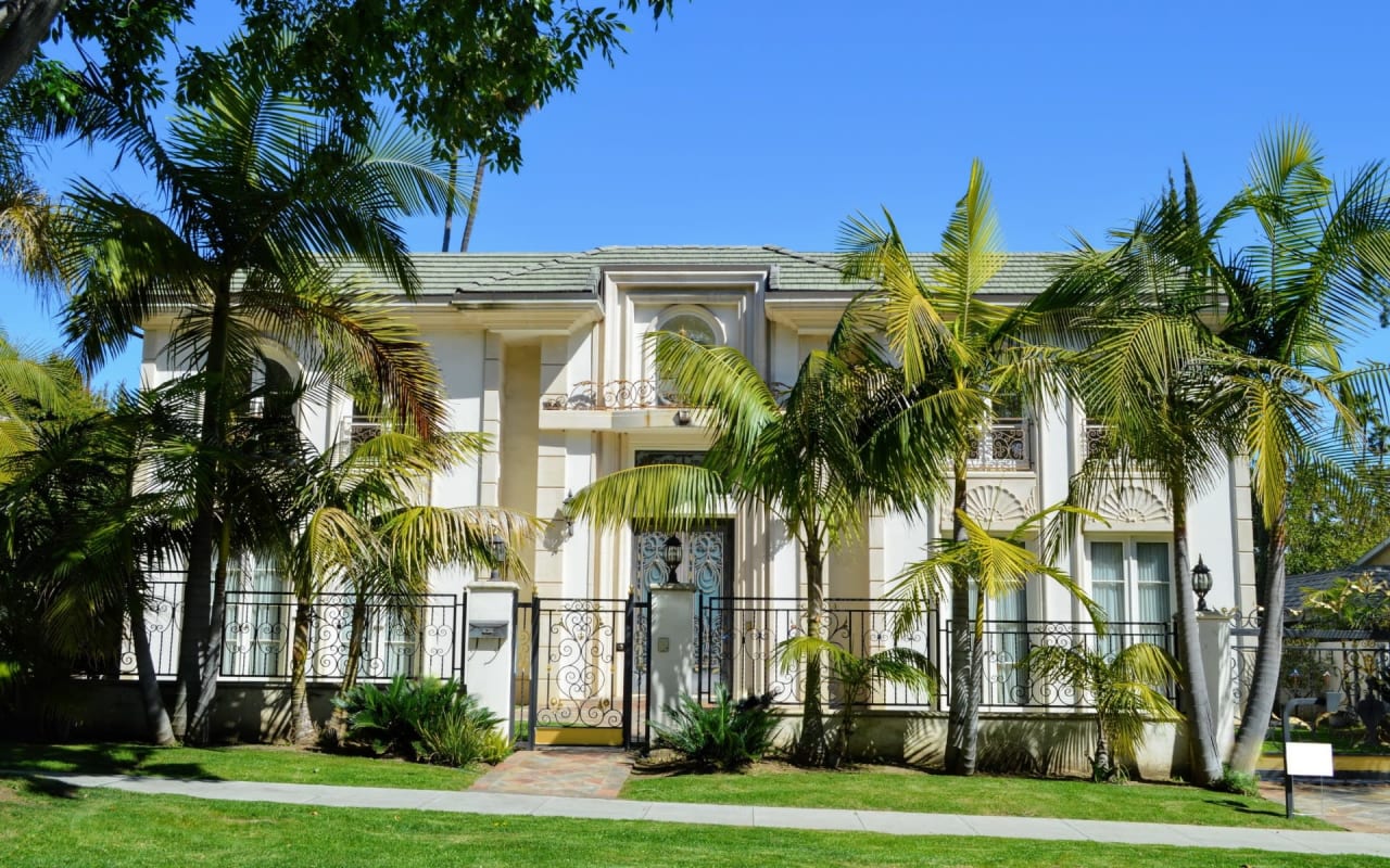  A large white house surrounded by palm trees and a fence