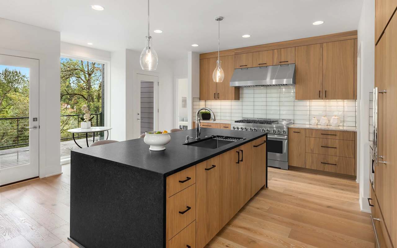 Modern kitchen with warm wood cabinets, a large black island, and a tree-lined balcony view.