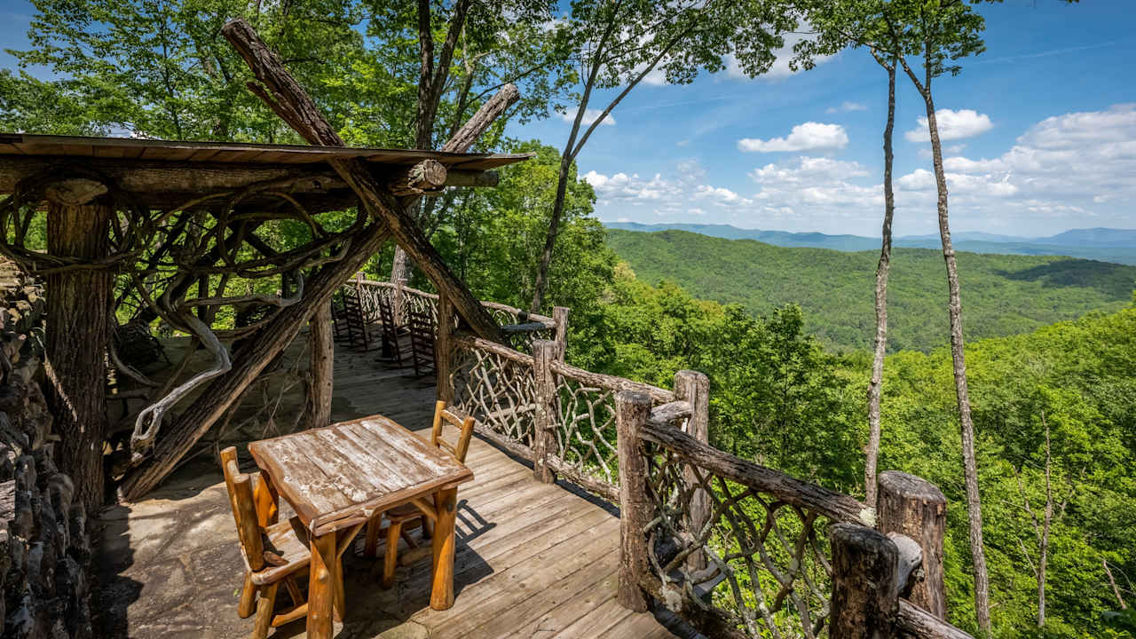 A wooden deck with a table and chairs overlooks a majestic mountain range. 