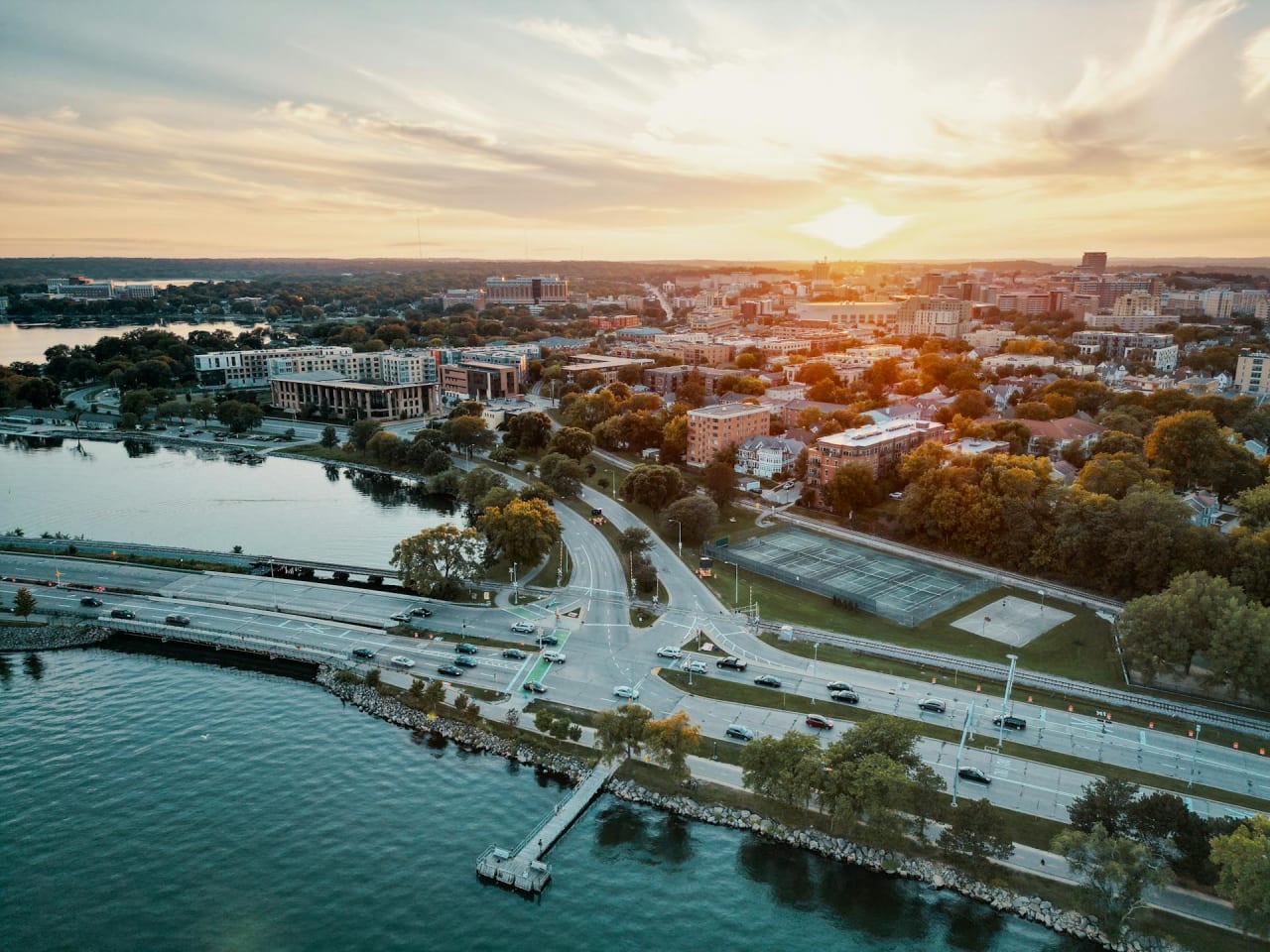 An aerial view of Madison, Wisconsin at sunset, surrounded by water and buildings of varying heights.