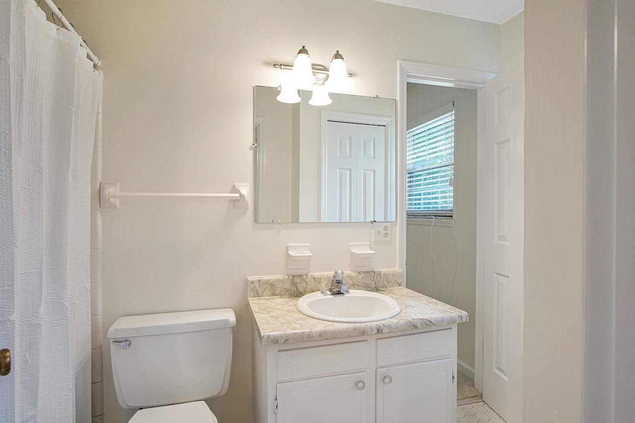 Photo of the Jack and Jill bathroom featuring a bathtub, a towel rack, a toilet, a single vanity, a modern light fixture, a mirror, and a white vanity