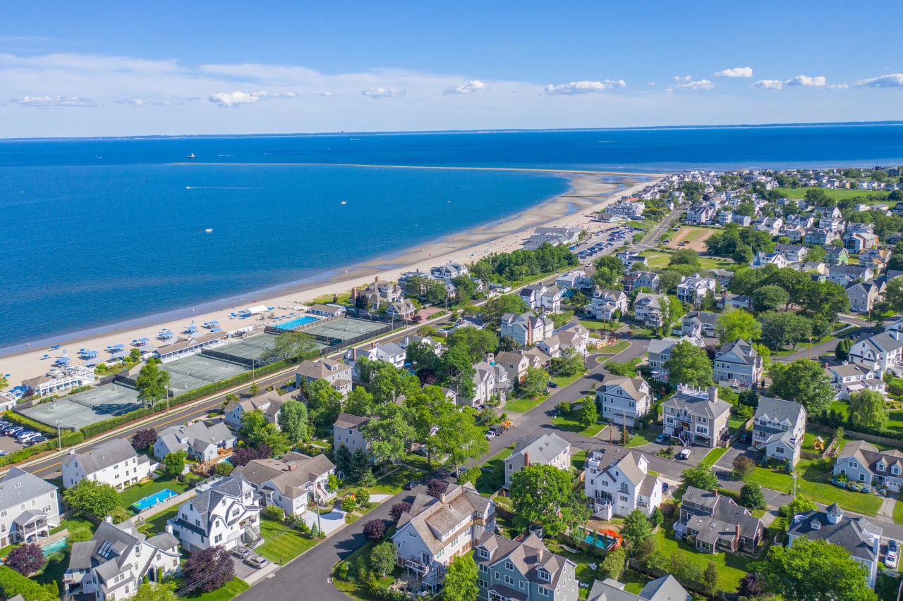 An aerial view of a residential neighborhood with a beach and a tennis court.