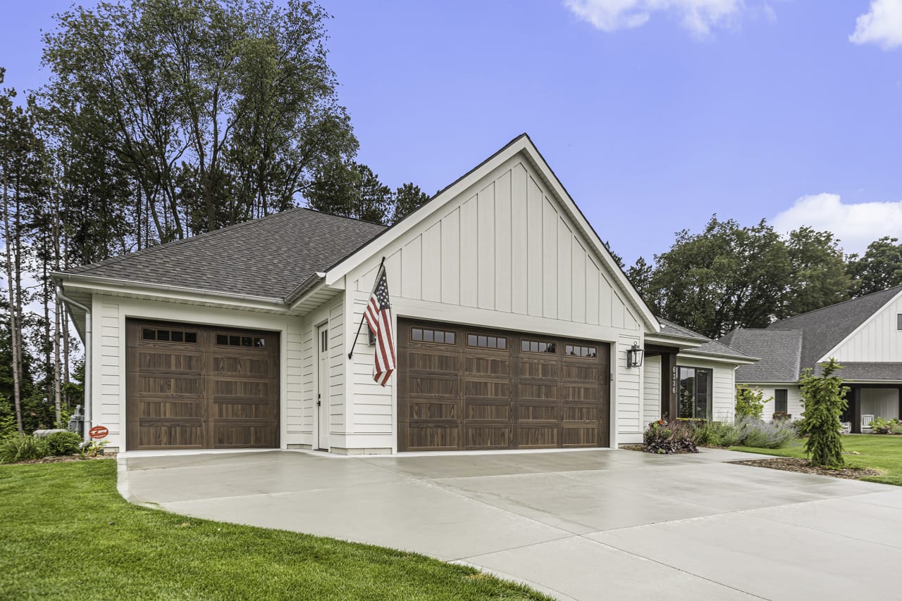 A white house with a brown garage door and American flag in a sunny day