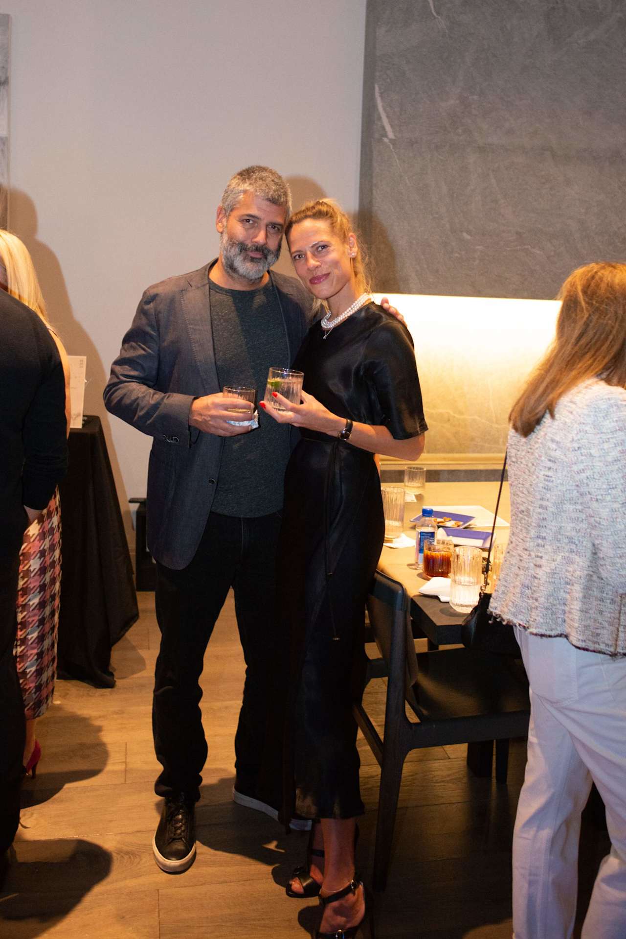 Two guests pose with drinks at an indoor gathering.