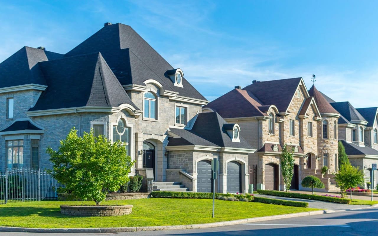 A row of large two-story diverse townhouses with front yards in a quiet residential area.