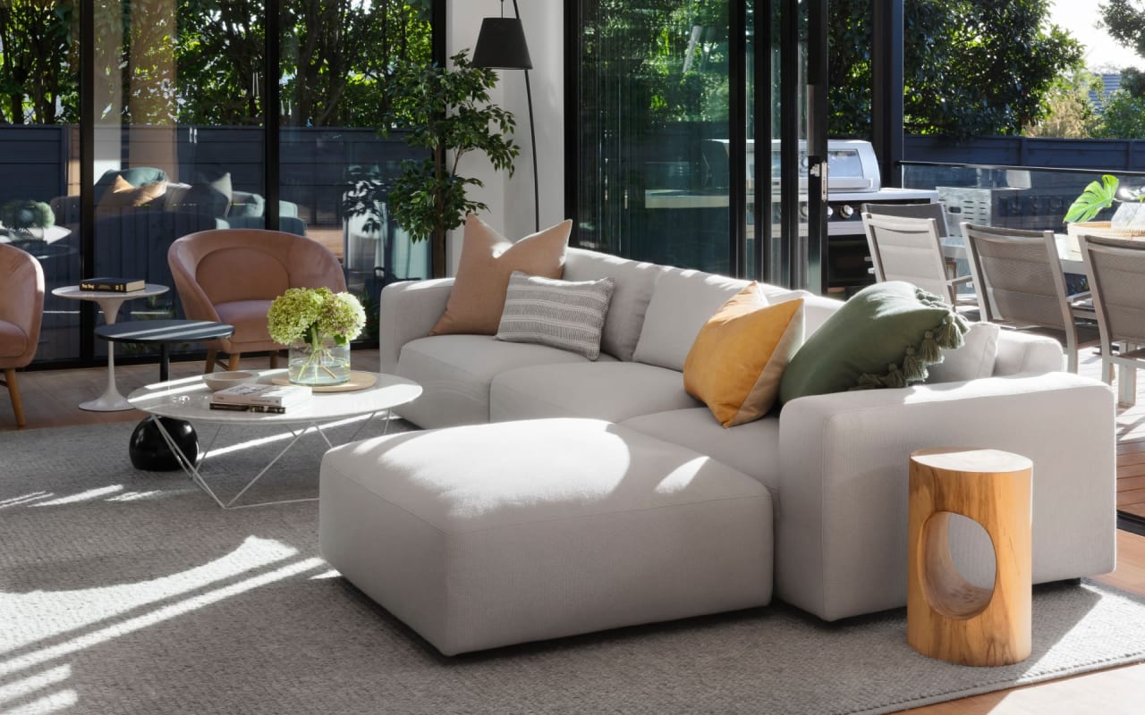 A bright and cheerful living room with a gray couch, glass coffee table, and gray carpet.