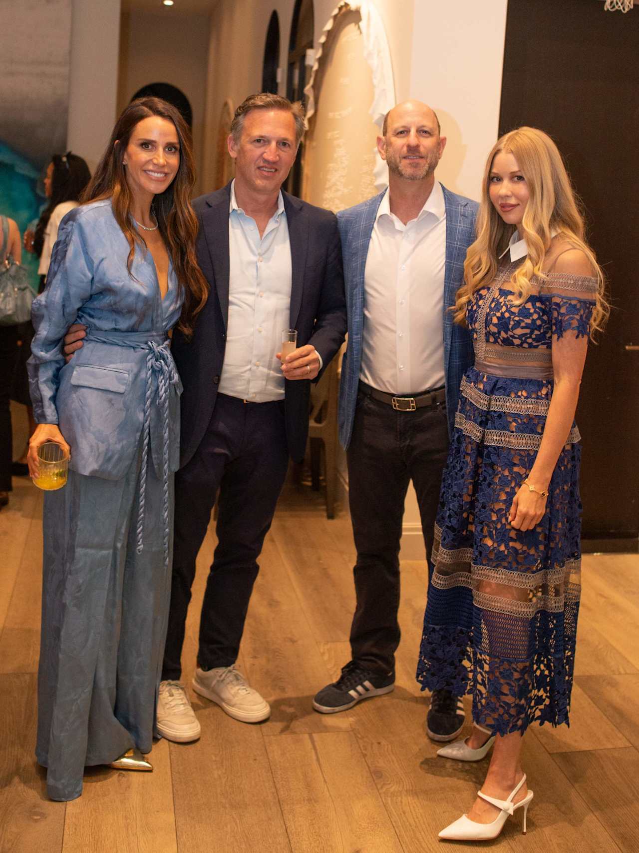 Four adults pose together at an indoor event, with a wedding dress displayed behind them.