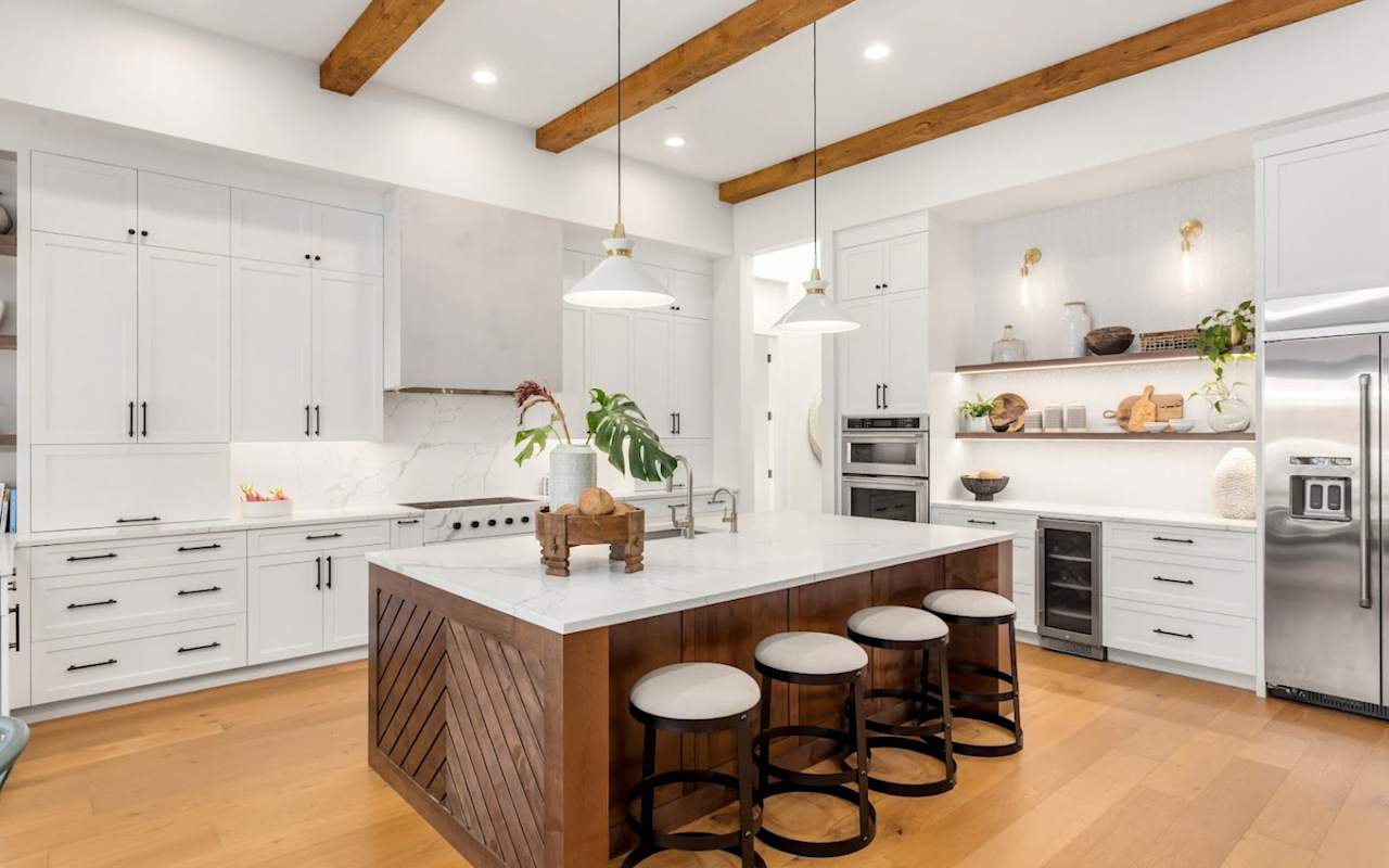 A modern kitchen with wood accents, featuring a large island with bar stools, stainless steel appliances, and open shelving.