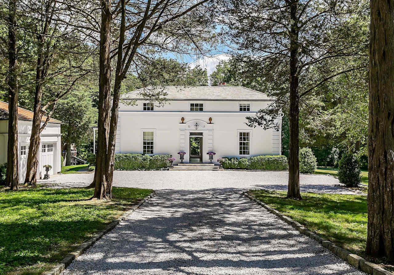 A winding gravel driveway leads up to a large white house.