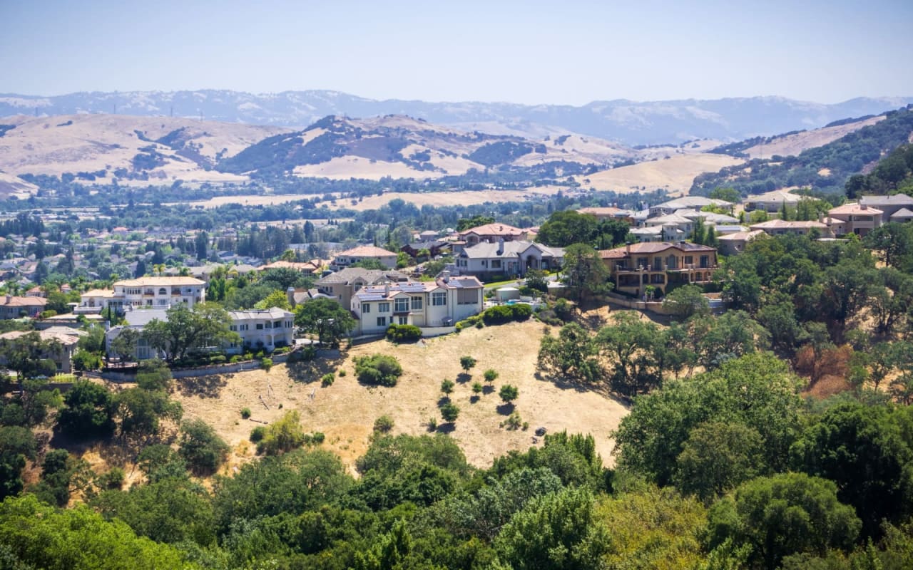 A residential area on a hill with mountains in the background.