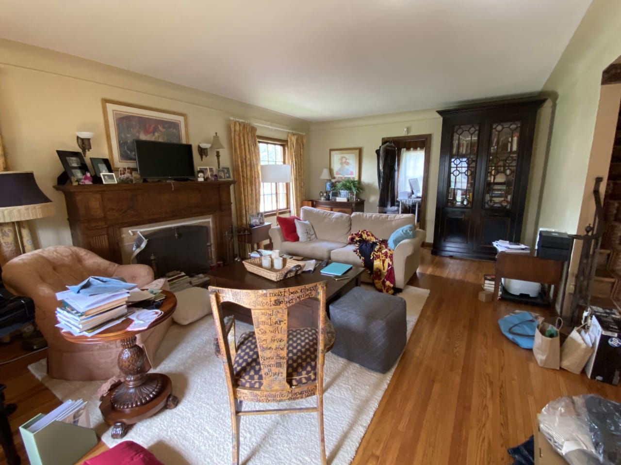 A messy living room with a couch, chairs, a fireplace, and a television placed on top of the fireplace.