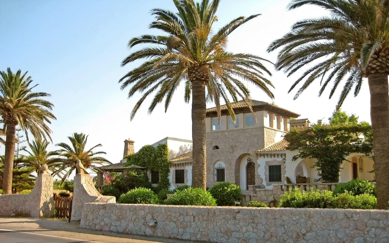 A large white house that is surrounded by palm trees and a lush green lawn