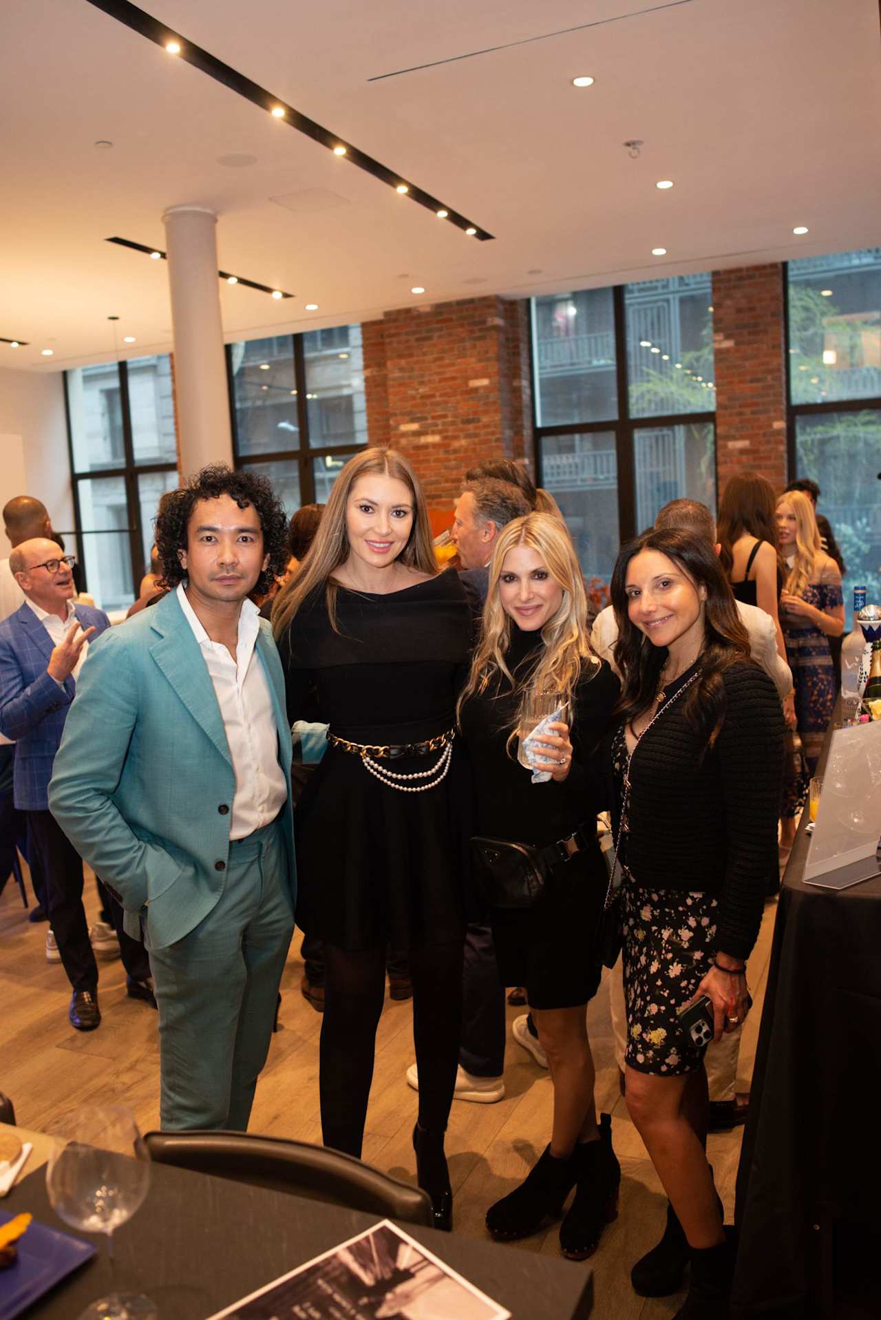 Four attendees pose together at an indoor event, surrounded by a crowd of guests.