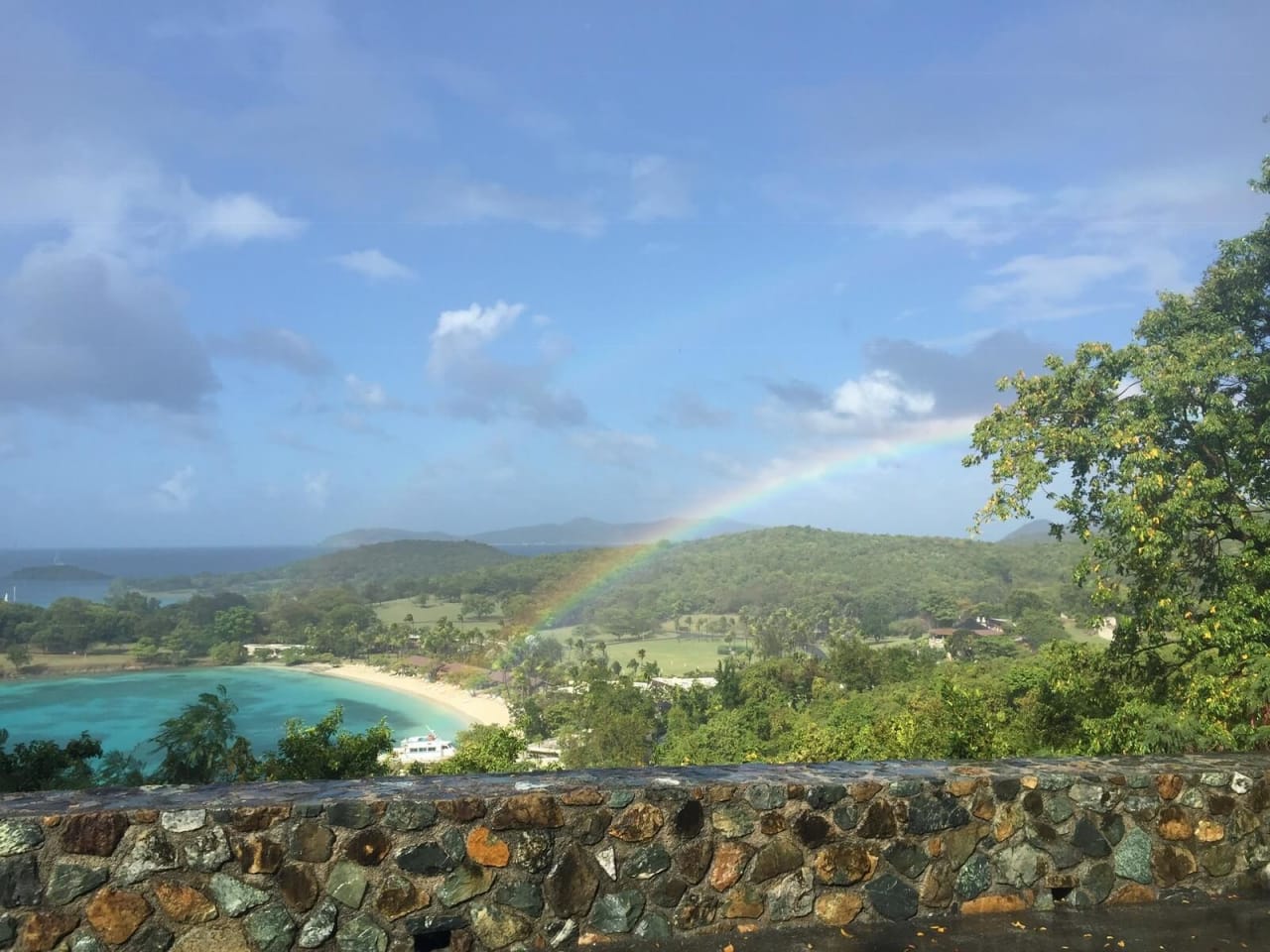 A vibrant rainbow arcs across a secluded beach, its colors reflected in the calm turquoise waters