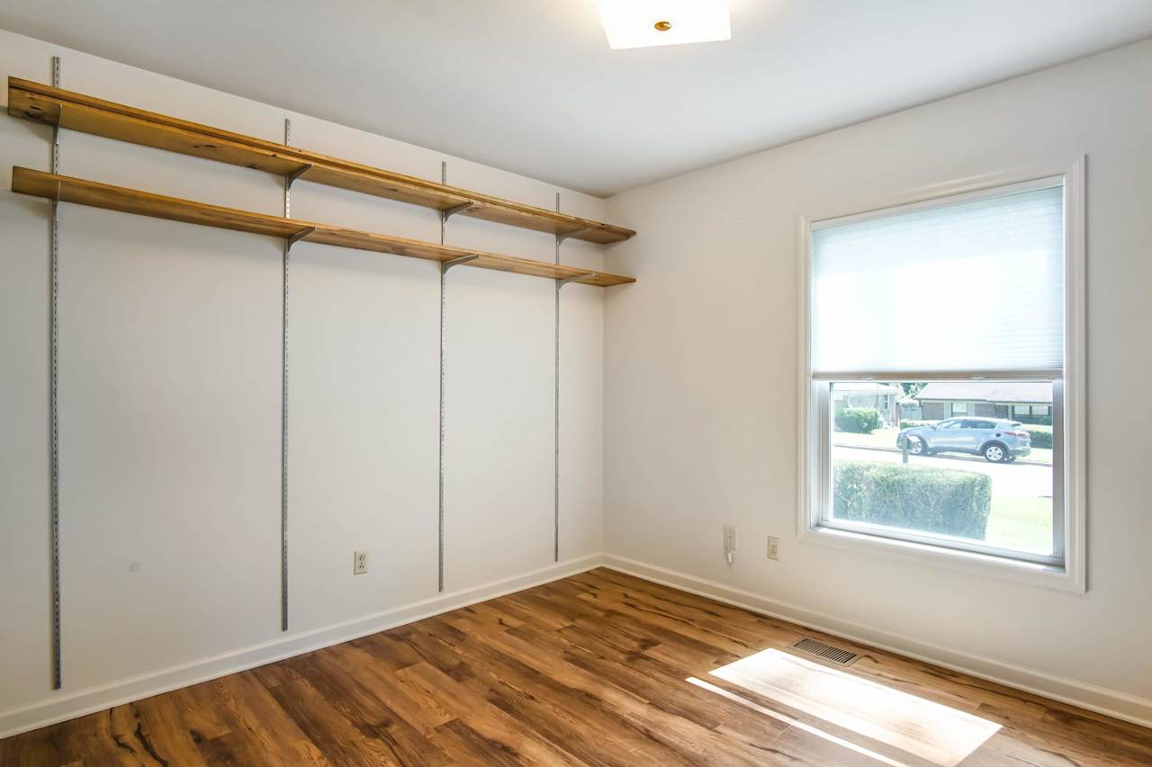 Photo of the second bedroom featuring modern built in shelving, plank flooring, white walls, a simple light fixture, and a window at 1228 Winifred Drive, Tallahassee, Florida 32308