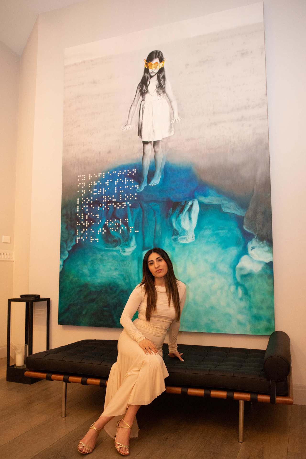 Woman in a cream dress seated on a black bench before a large turquoise artwork.